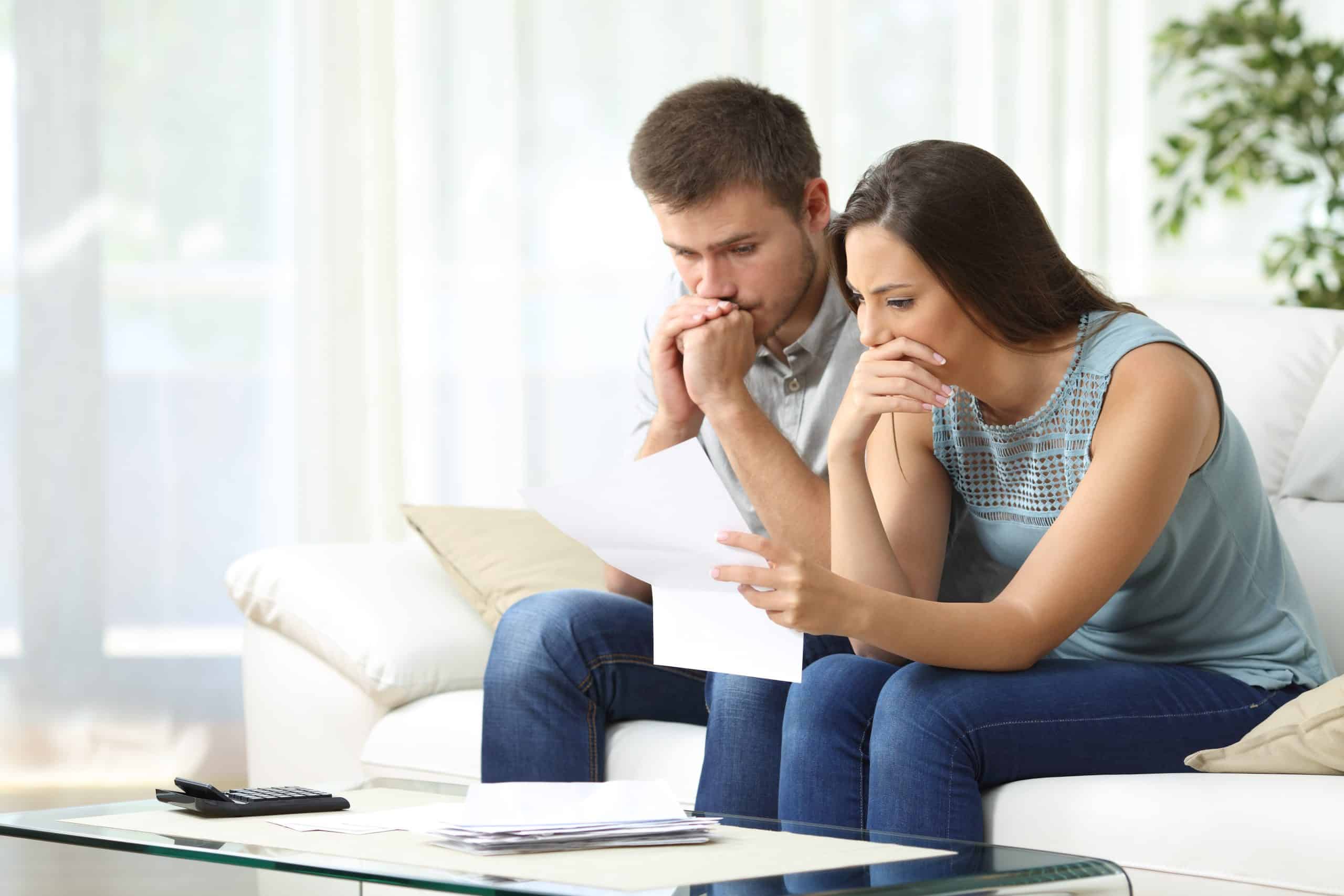anxious couple sitting together on a couch, looking worried while reading a lawsuit document